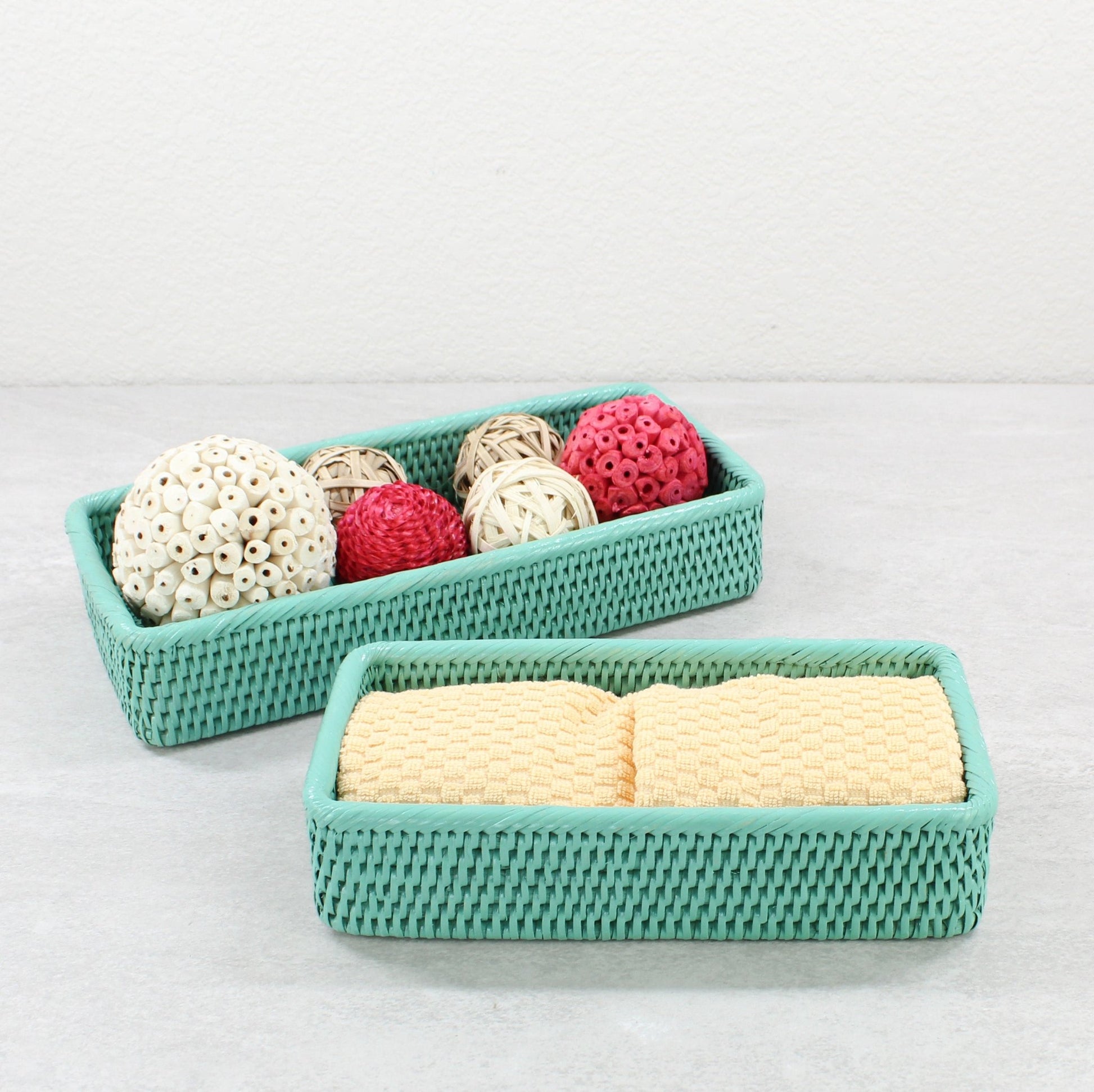 Turquoise rectangular rattan trays holding yellow towels and decorative balls on a gray bathroom counter.