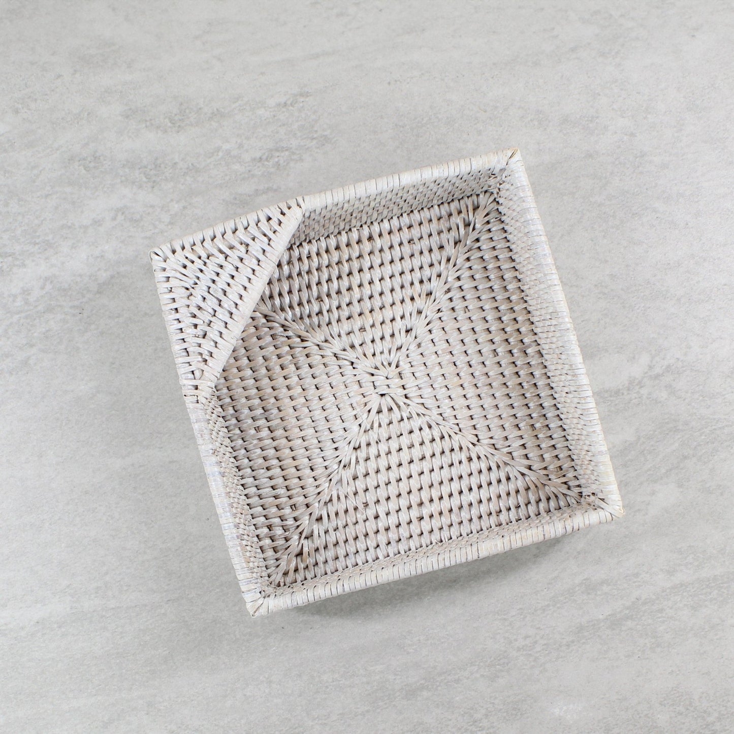 Whitewash handwoven rattan napkin holder on a grey surface.