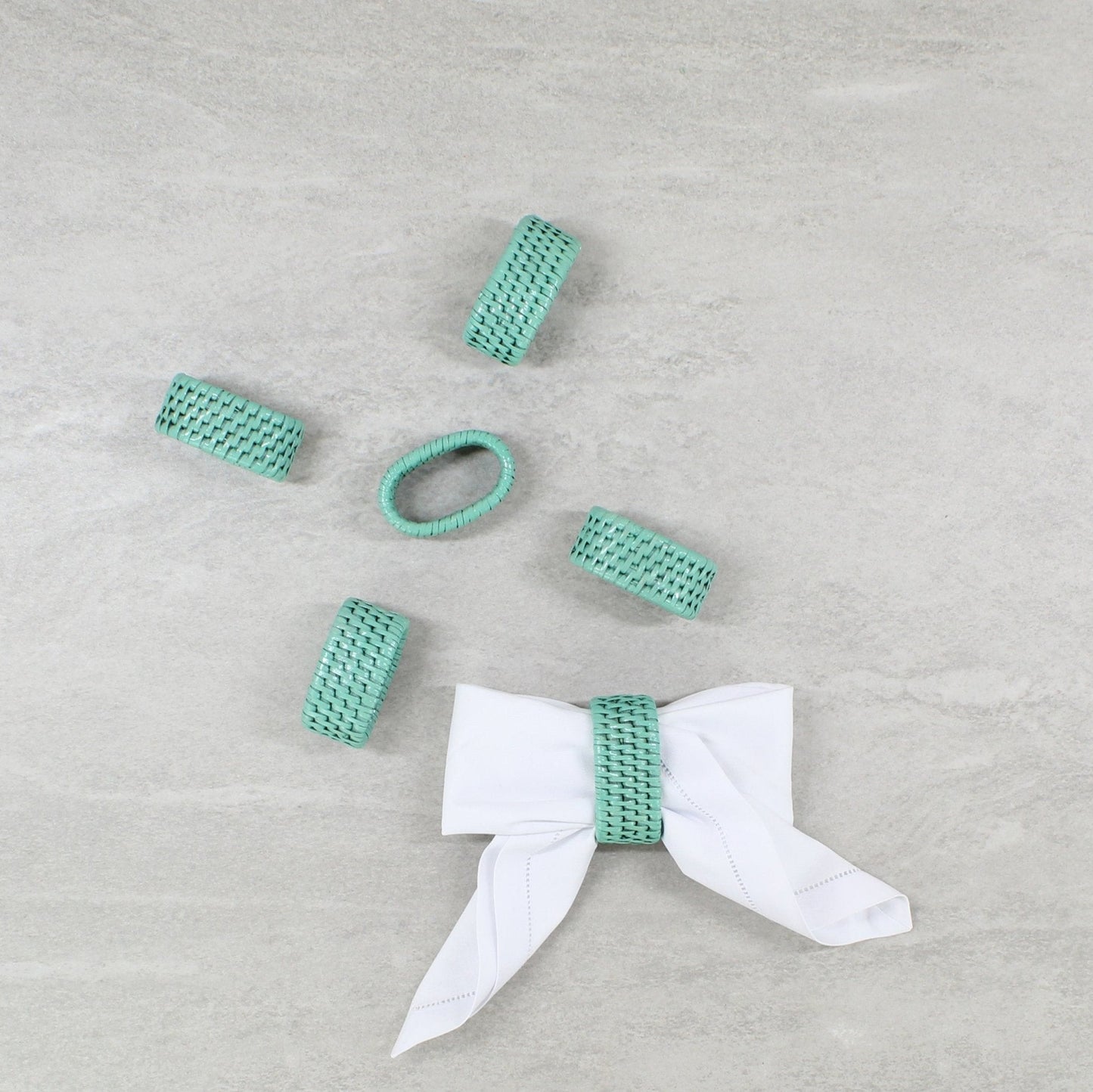 Set of six turquoise handwoven rattan napkin rings with one styled around a bow—adds charm to coastal or tropical table settings.