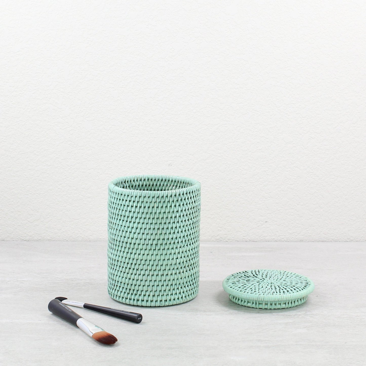 Sage leaf green woven rattan canister basket with a lid on a light background