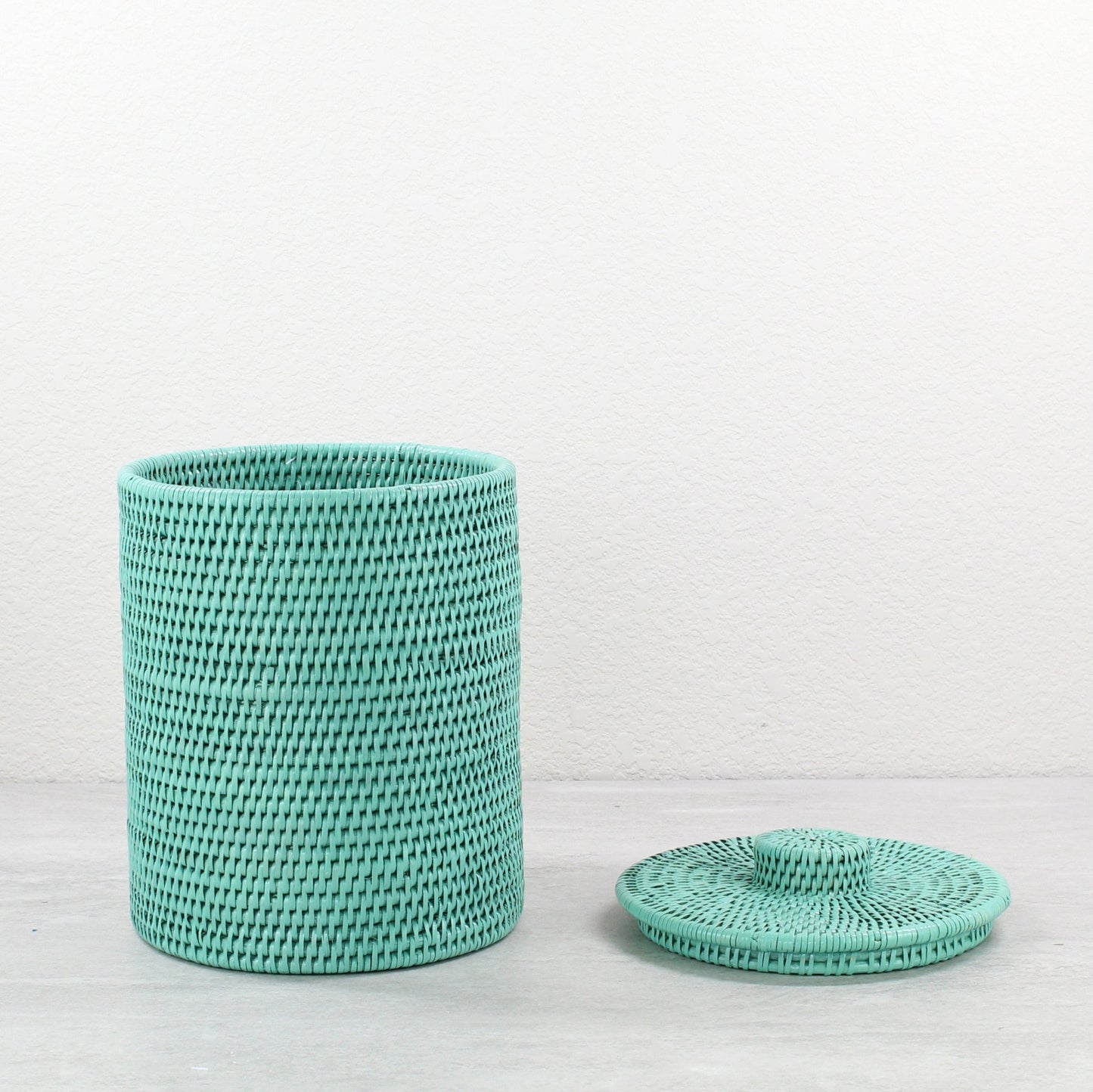 Tall round turquoise rattan canister with woven lid, shown with lid placed beside the base