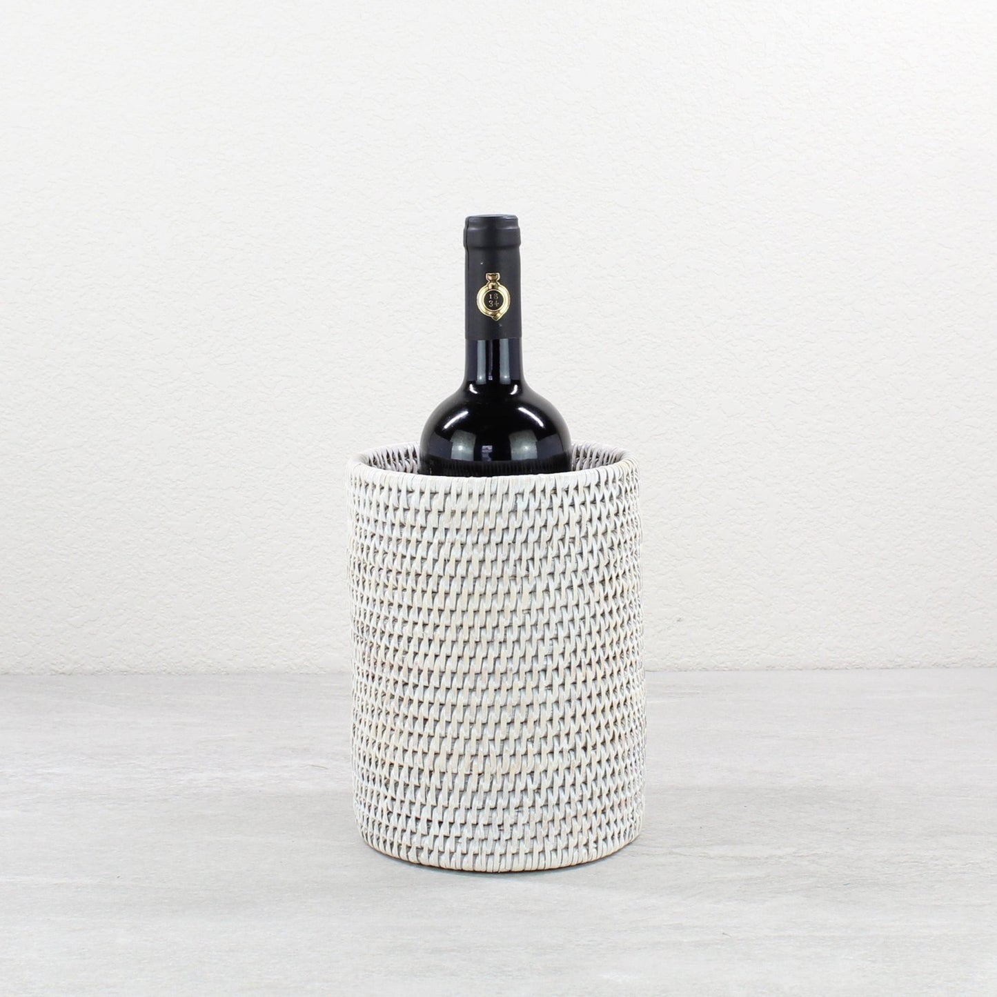 Handwoven whitewash rattan wine holder with a bottle of wine on a light gray background