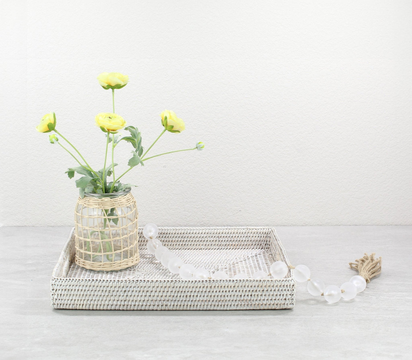 Handwoven white rattan tray with a vase of yellow flowers and frosted bead garland for natural modern home décor