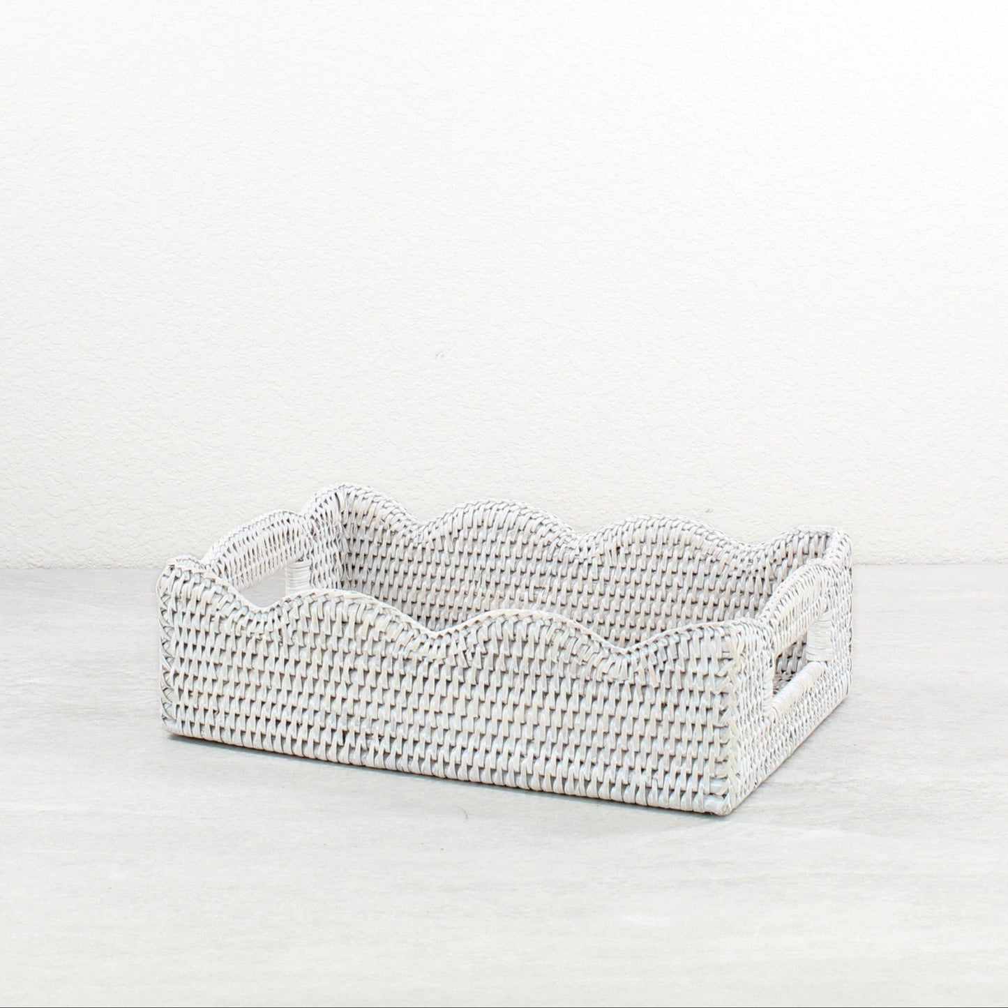 Handwoven rectangular scalloped rattan basket on a light gray background