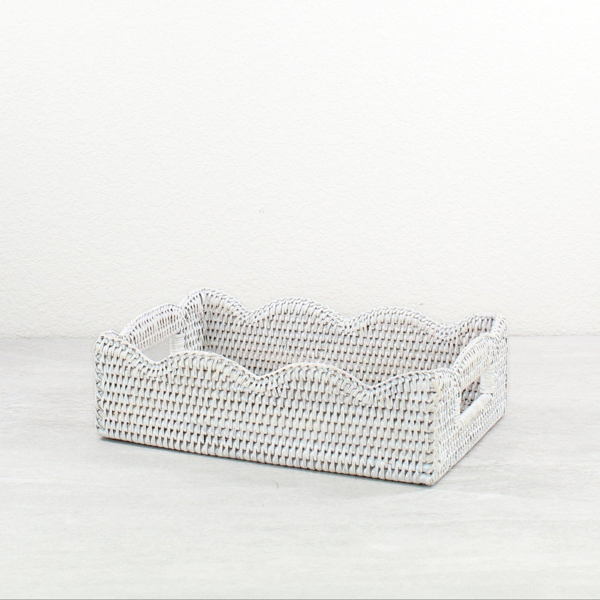 Handwoven rectangular scalloped rattan basket on a light gray background
