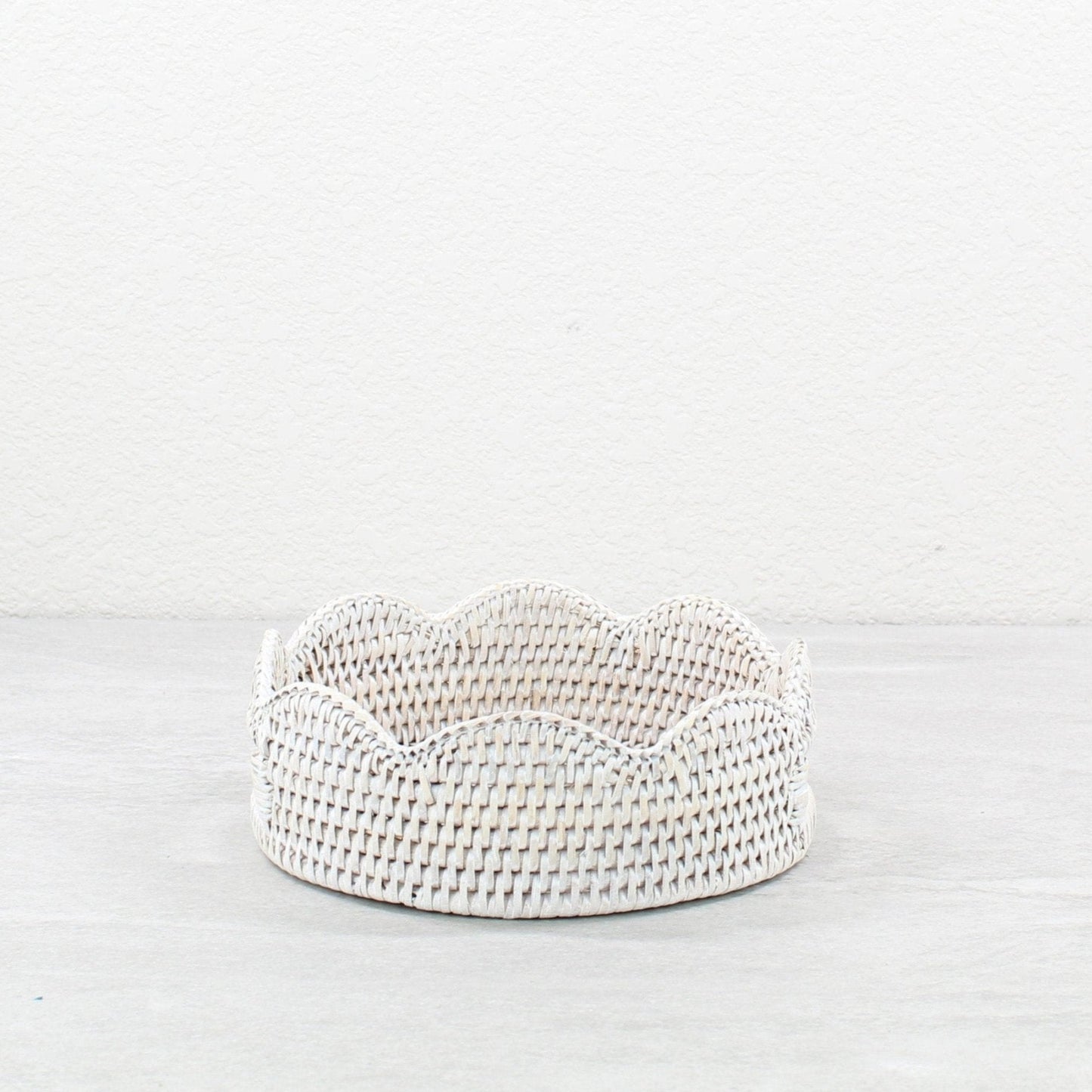 Round whitewashed rattan tray with scalloped edge, handwoven for elegant countertop or tabletop storage.
