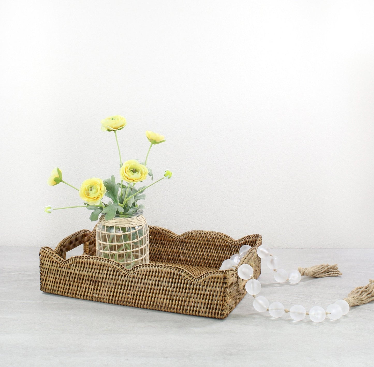 Honey brown medium scalloped rattan tray styled with a woven vase and yellow flowers, perfect for dining table or entryway centerpiece.