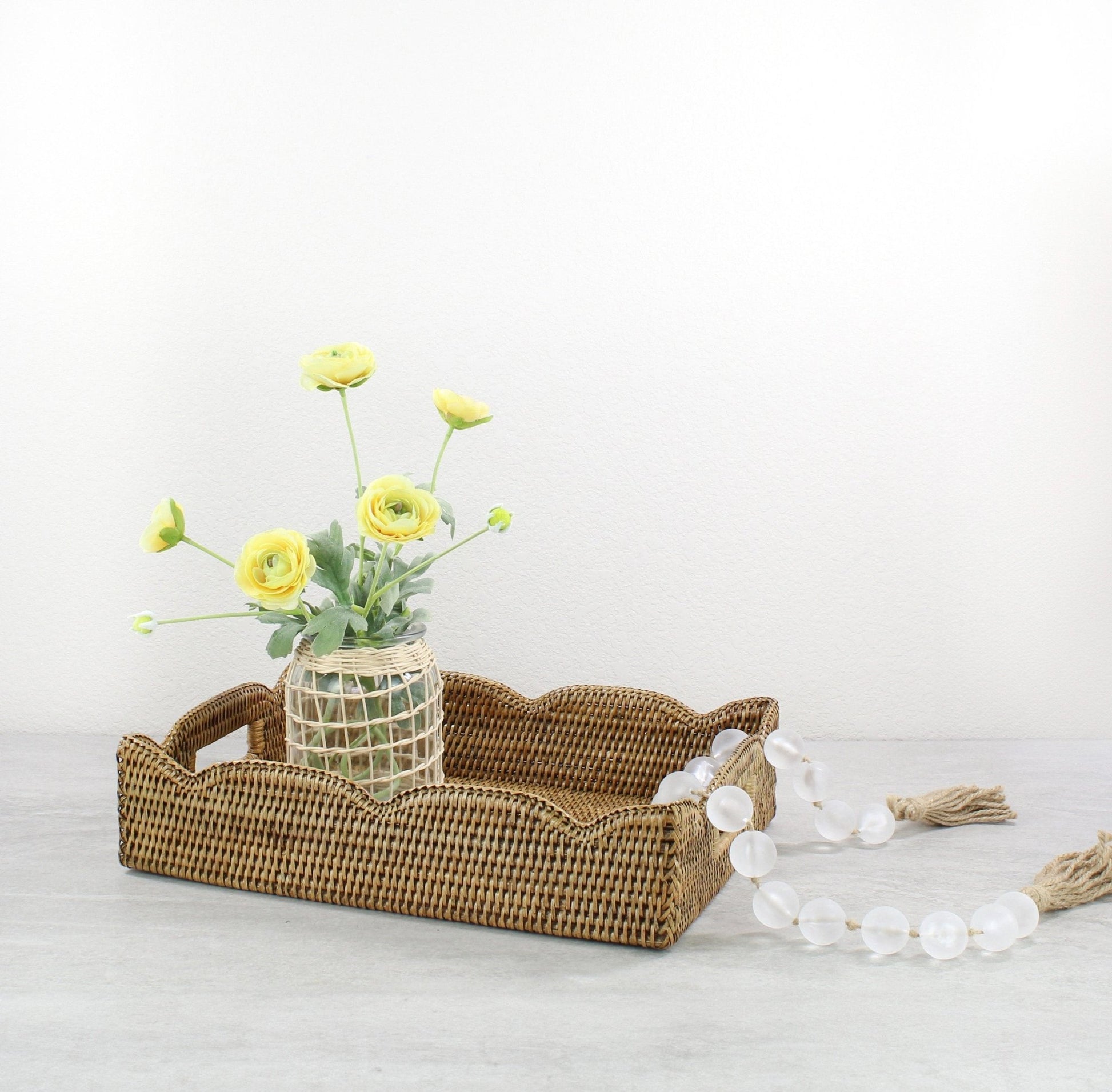 Honey brown medium scalloped rattan tray styled with a woven vase and yellow flowers, perfect for dining table or entryway centerpiece.