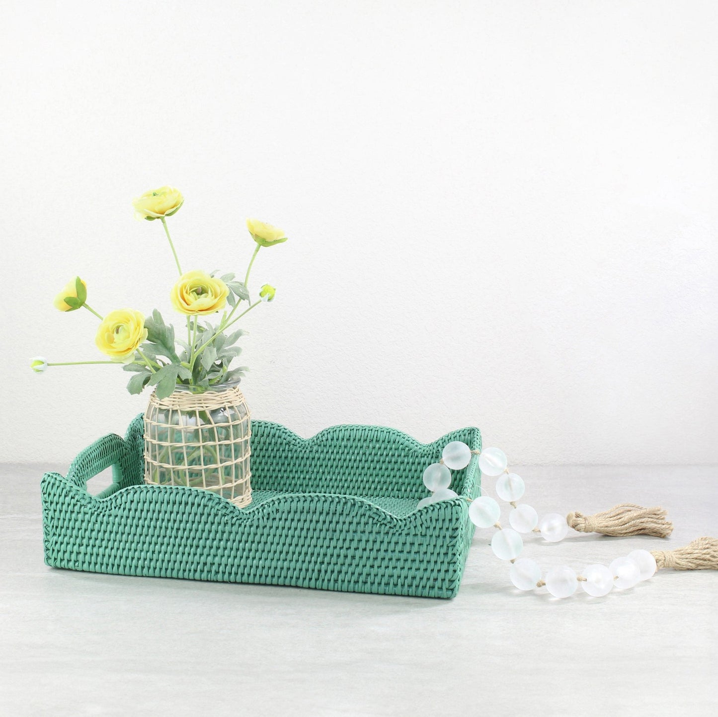 Turquoise scalloped rattan tray styled with woven vase of yellow flowers and glass bead garland, handmade eco-friendly decorative accent.
