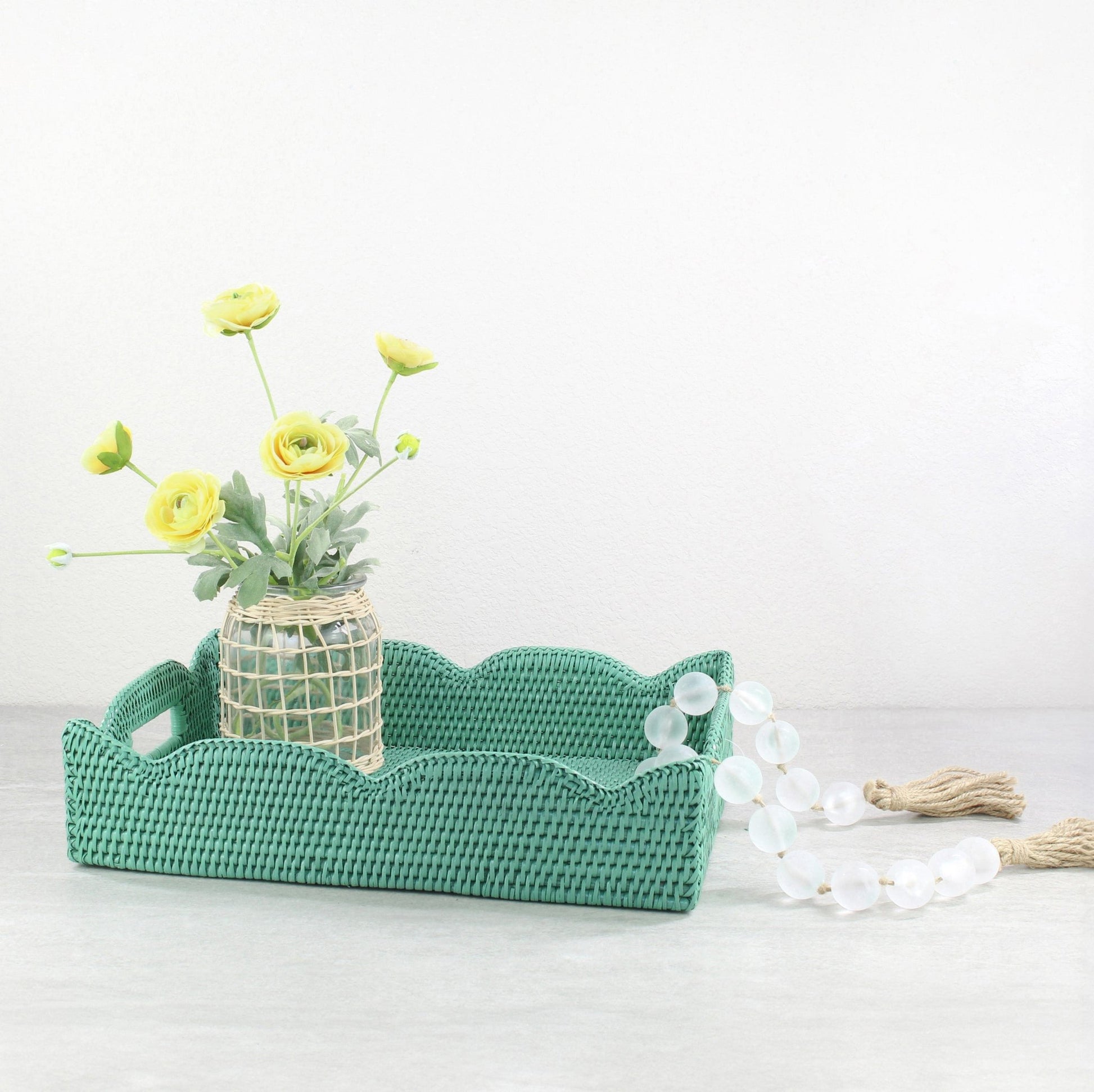 Turquoise scalloped rattan tray styled with woven vase of yellow flowers and glass bead garland, handmade eco-friendly decorative accent.