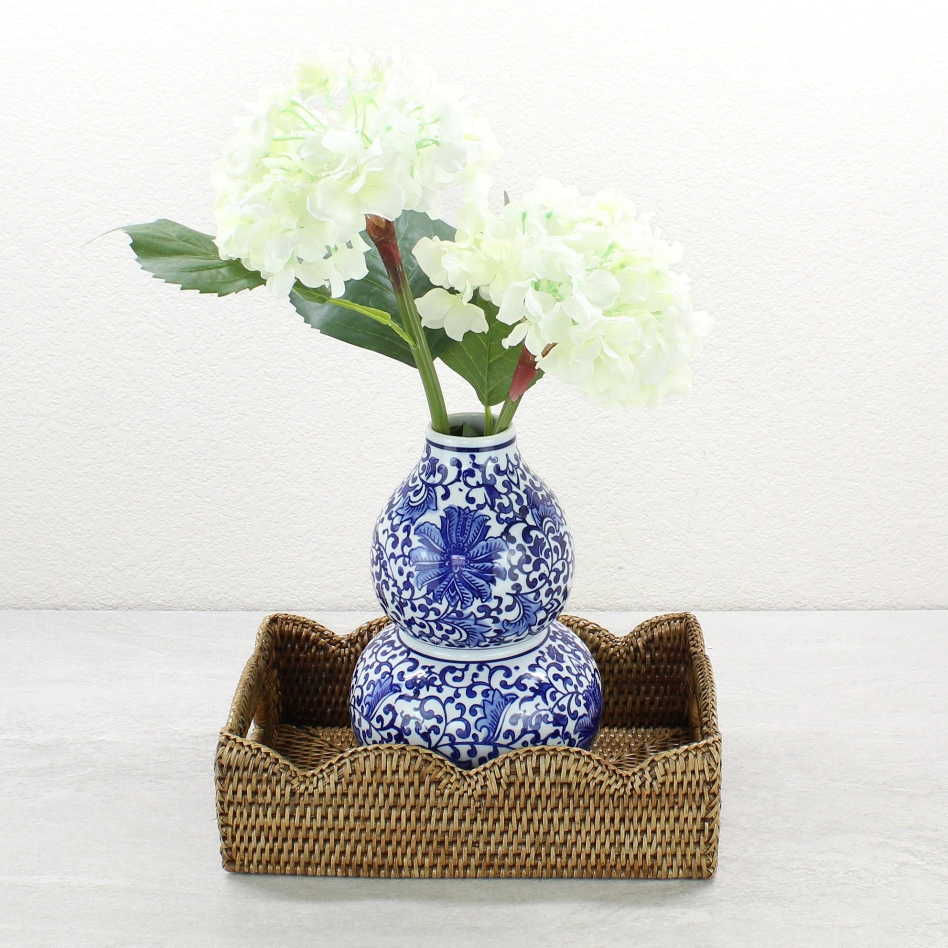 Small honey brown scalloped rattan tray holding ceramic vase on stone surface, styled for elegant and coastal home use.