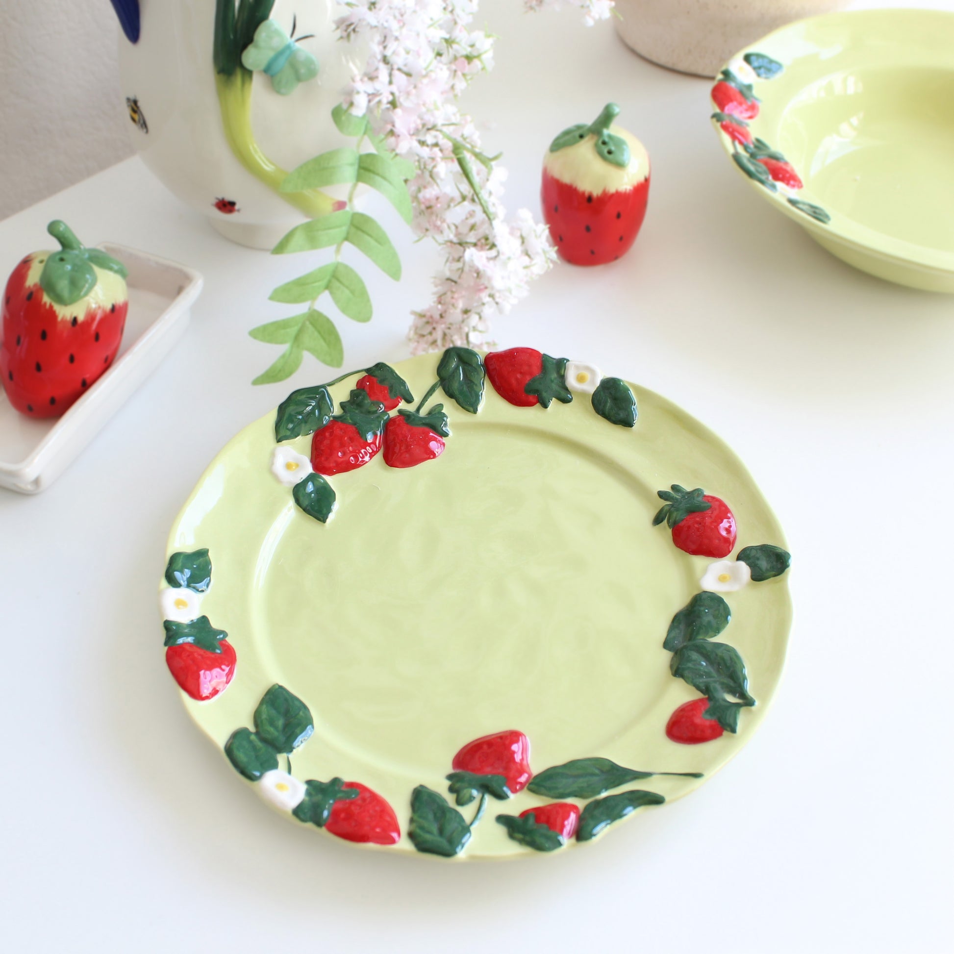 Strawberry embossed stoneware dessert plate styled on table with matching pasta bowl and shakers