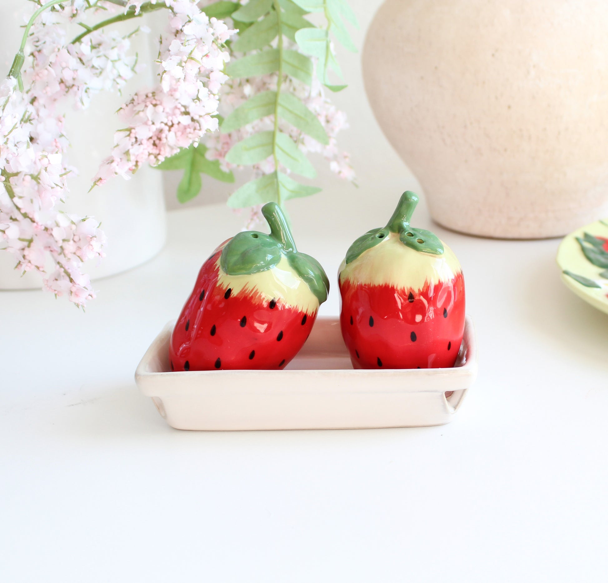 Pair of strawberry stoneware salt and pepper shakers in tray with floral background, farmhouse kitchen décor
