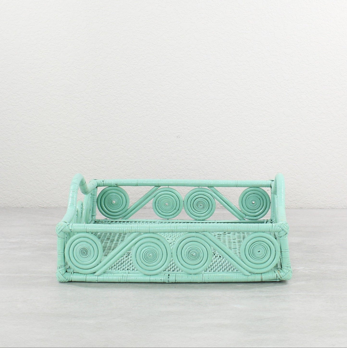 Square sage green rattan tray with swirly edges and curved handle, handwoven for eco-friendly storage.
