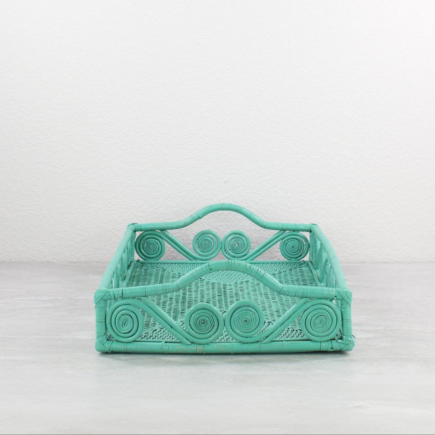 Empty turquoise rattan tray with swirl design and raised handles, displayed on a minimalist background.