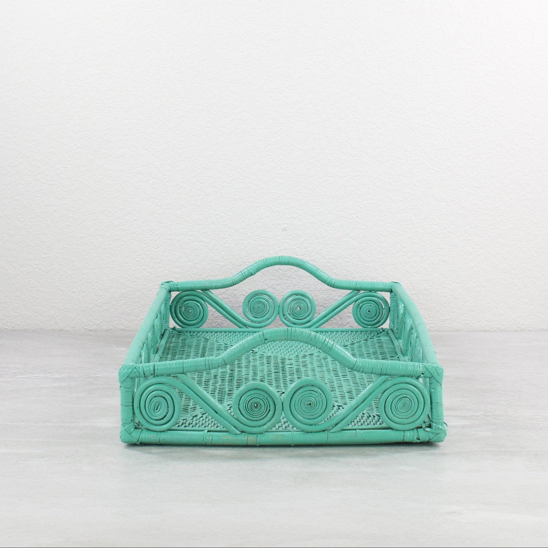 Empty turquoise rattan tray with swirl design and raised handles, displayed on a minimalist background.