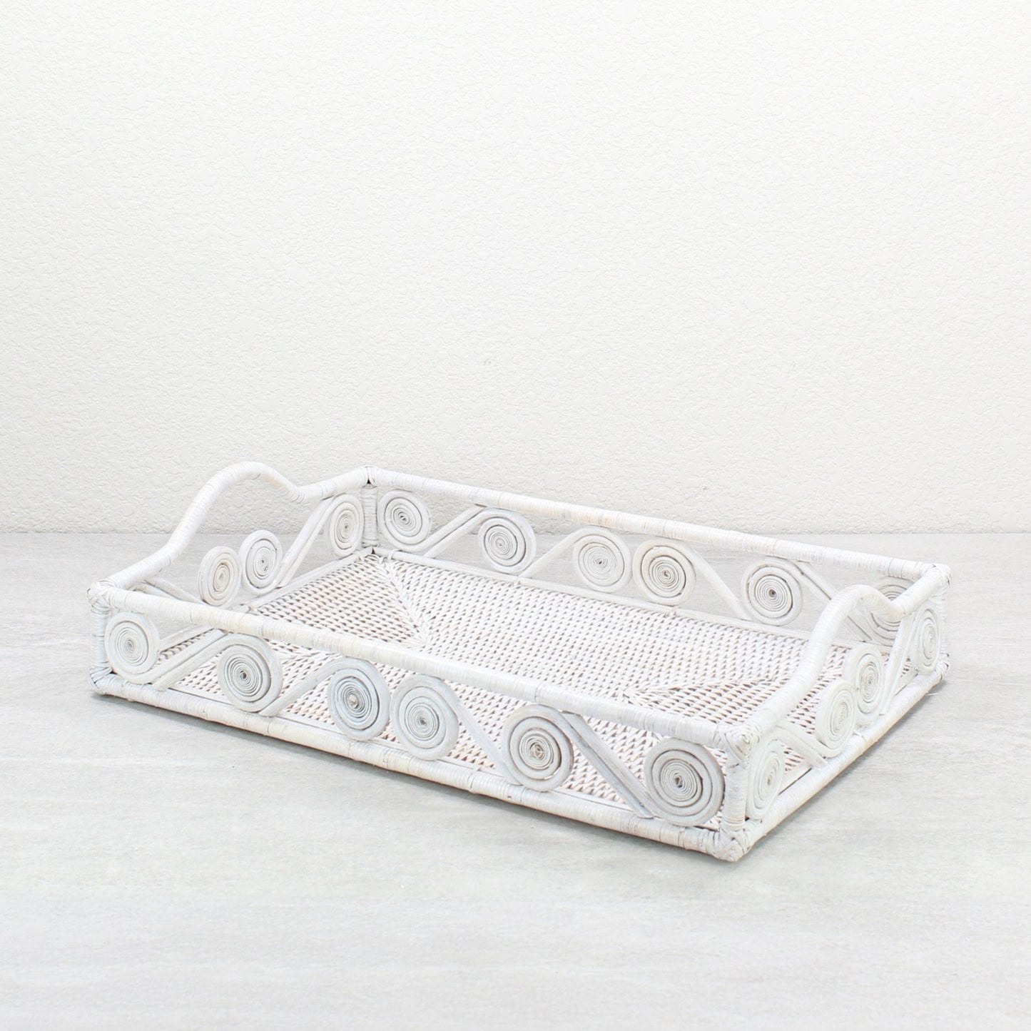 Empty whitewash rectangle rattan tray with swirl design and raised handles, handmade for serving or home décor.