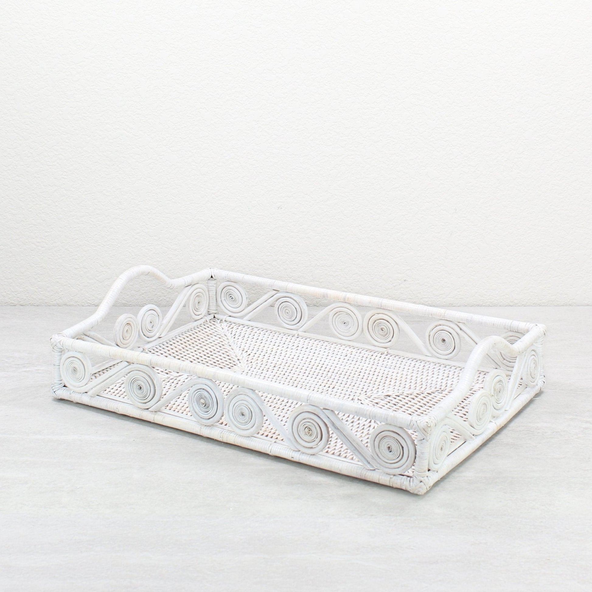 Empty whitewash rectangle rattan tray with swirl design and raised handles, handmade for serving or home décor.