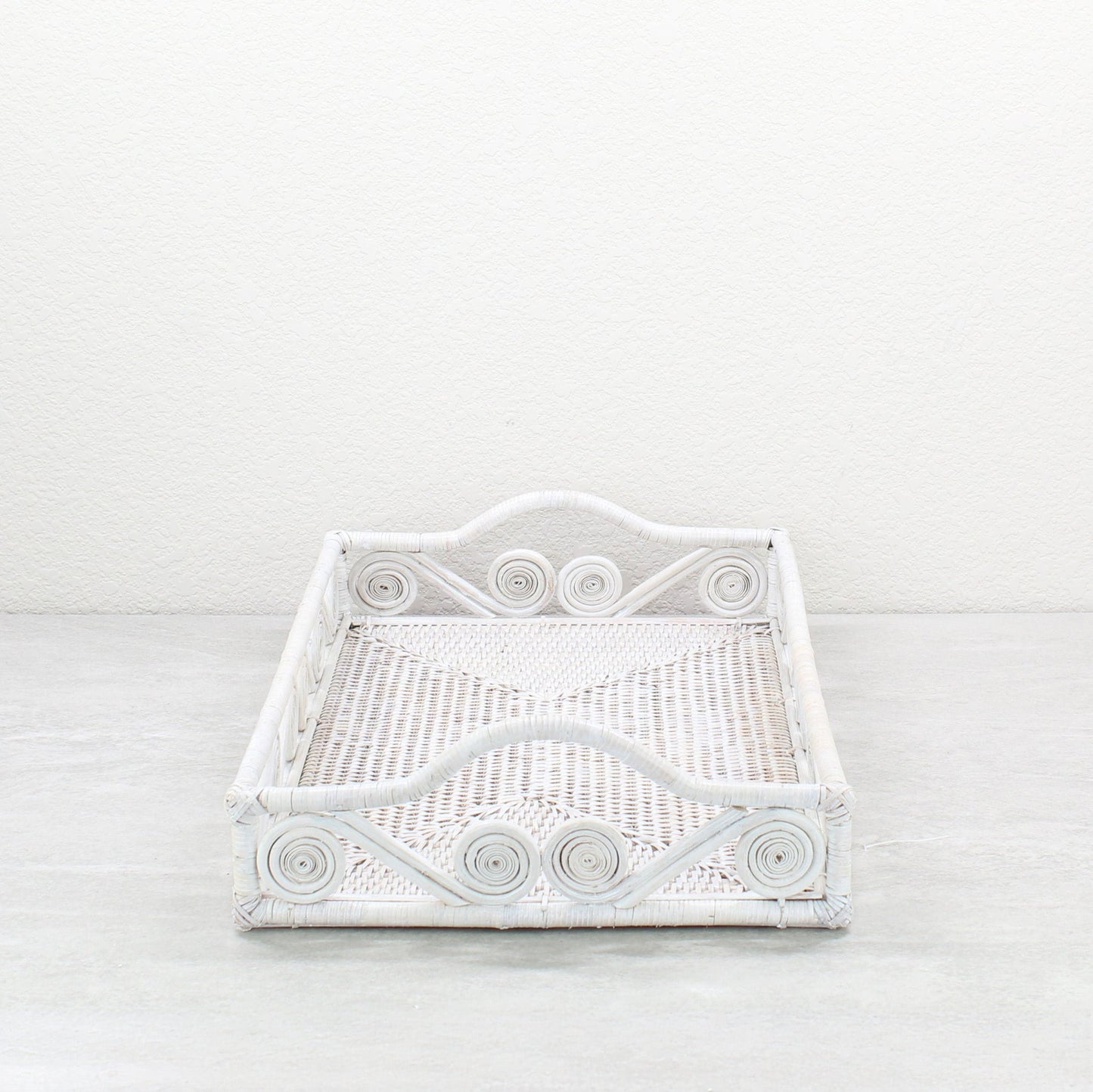 Empty white rattan tray with swirl design and raised handles, displayed on a minimalist background.