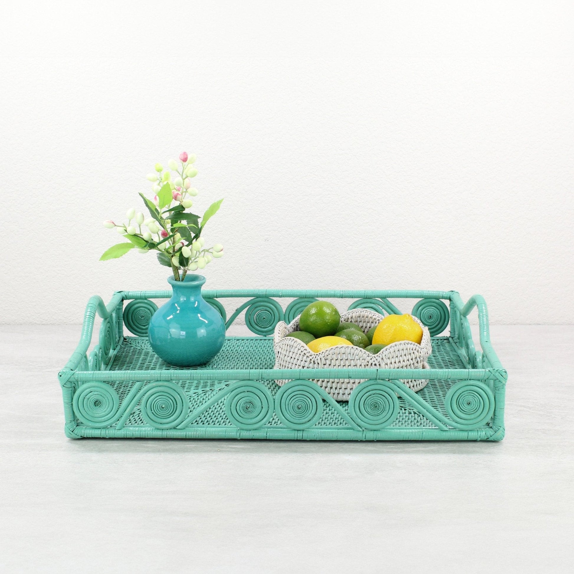 Turquoise rattan tray with swirl detail styled with a teal vase of flowers and a white rattan bowl of limes and lemons.