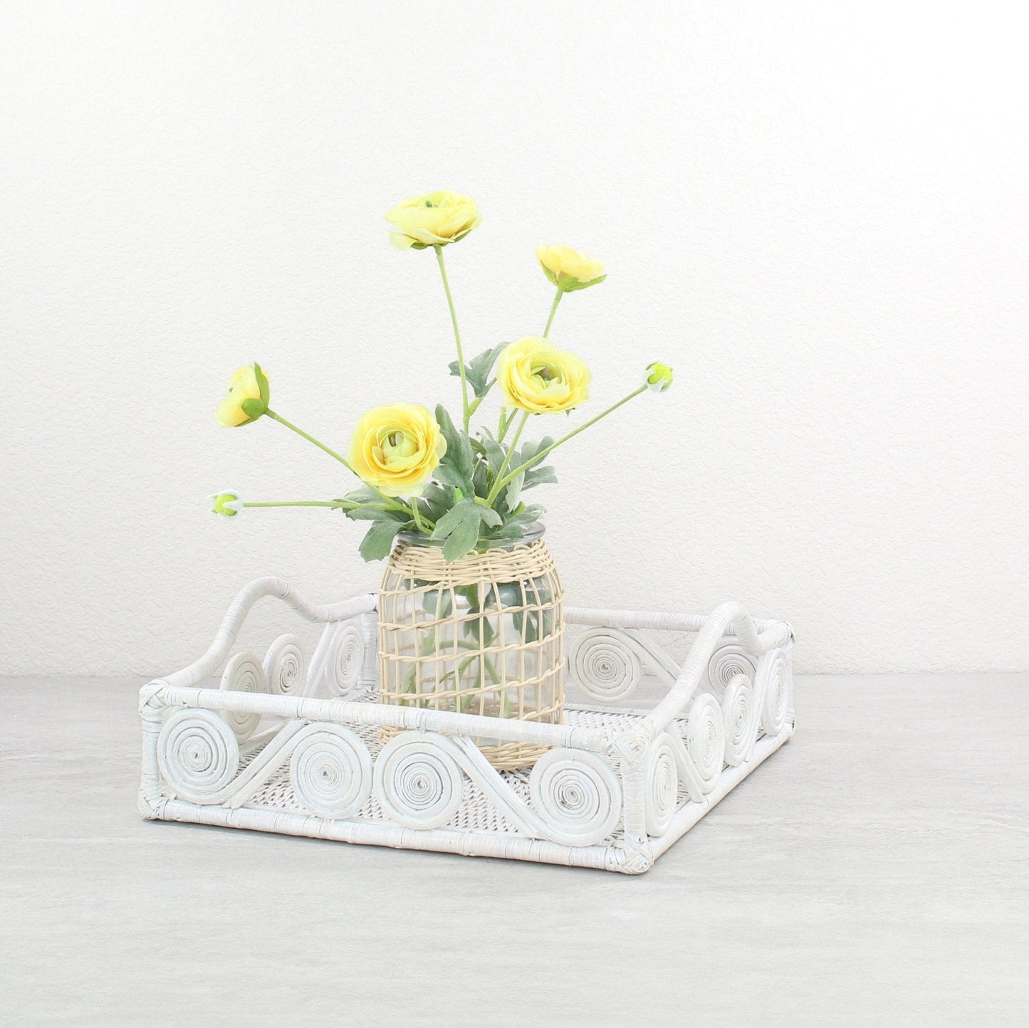 Whitewash rattan square tray styled with a woven vase of yellow ranunculus flowers on a neutral tabletop