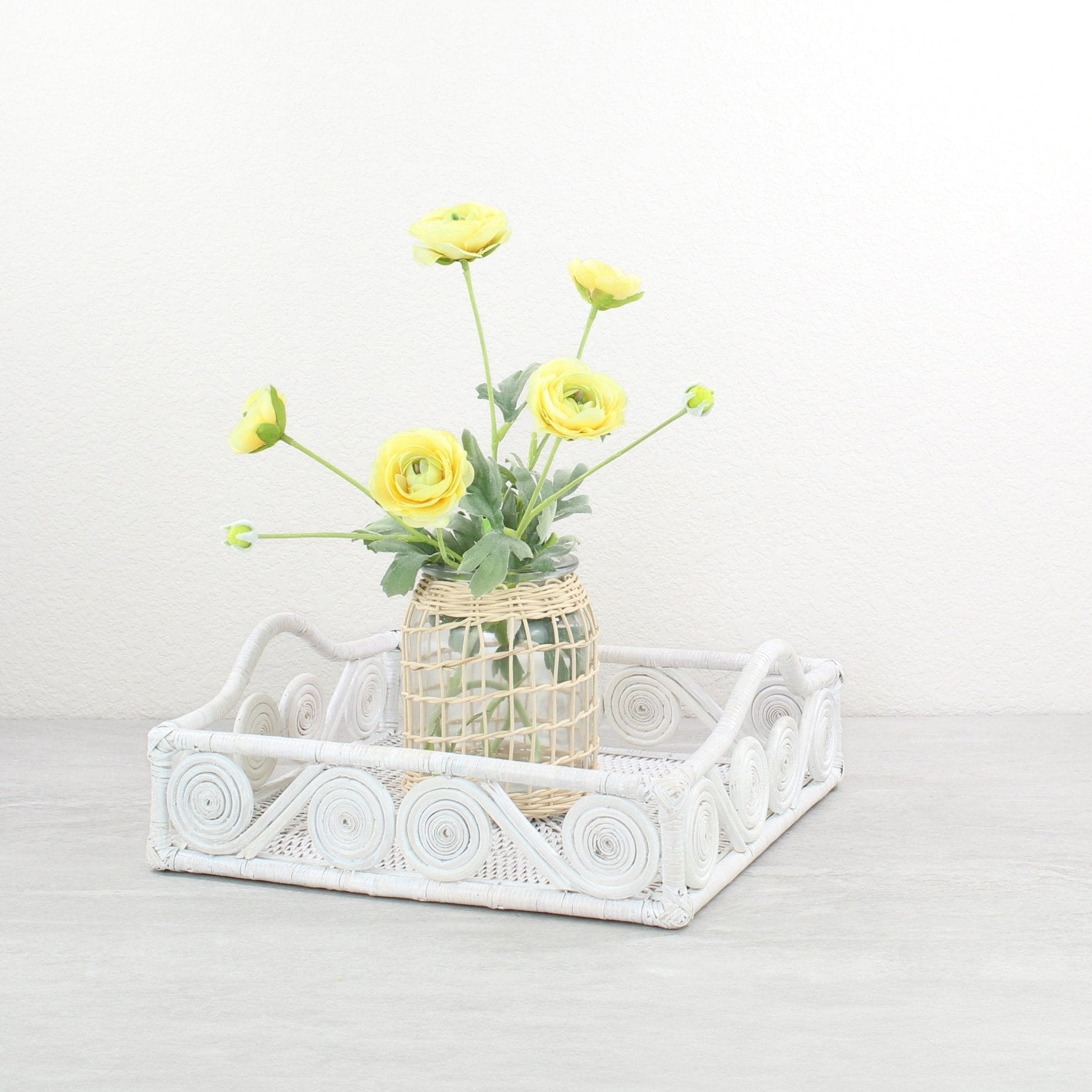 Whitewash rattan square tray styled with a woven vase of yellow ranunculus flowers on a neutral tabletop