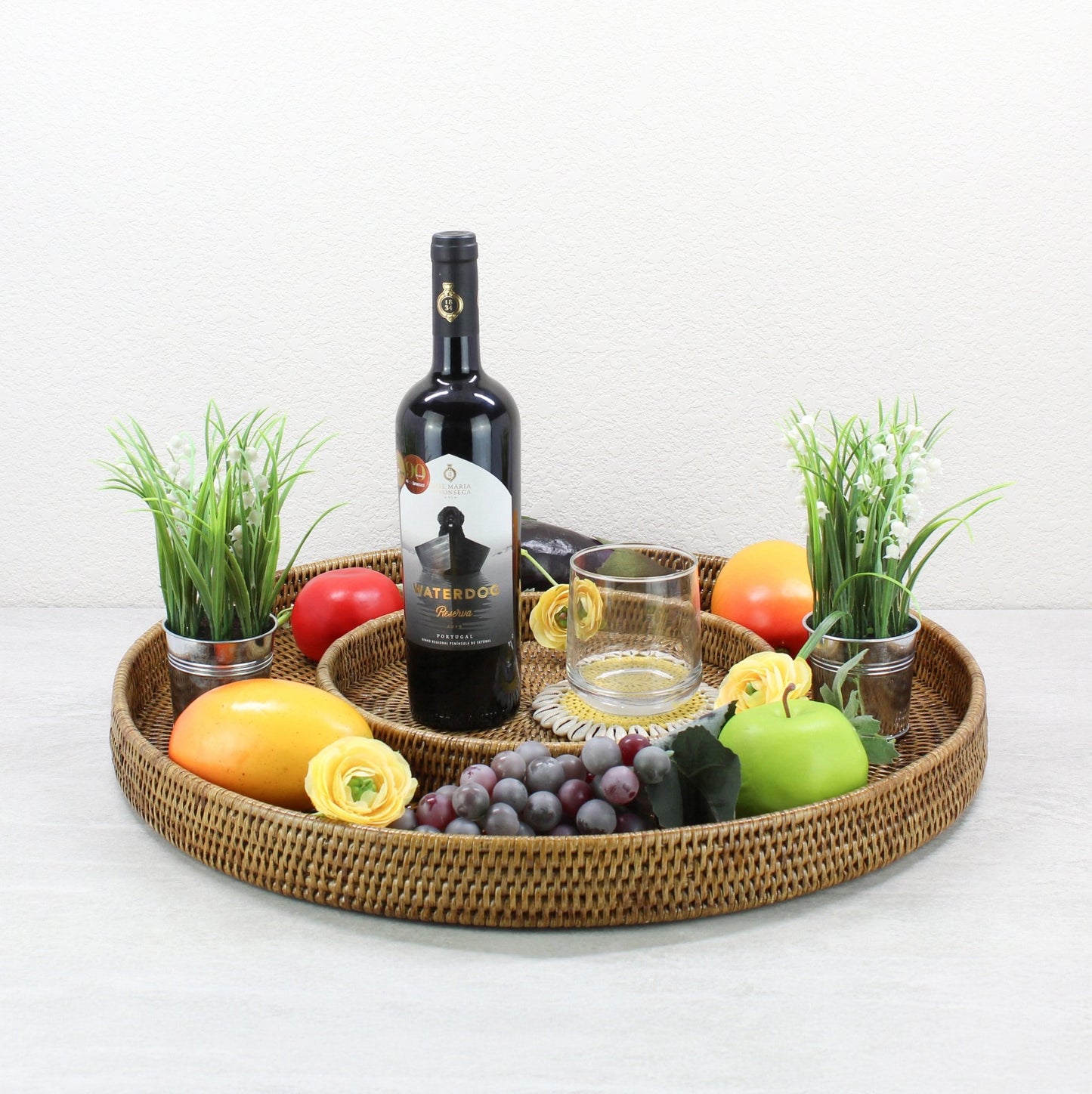 Round honey brown rattan tray styled with wine, glassware, fruit, and flowers, perfect for coffee table or bar display