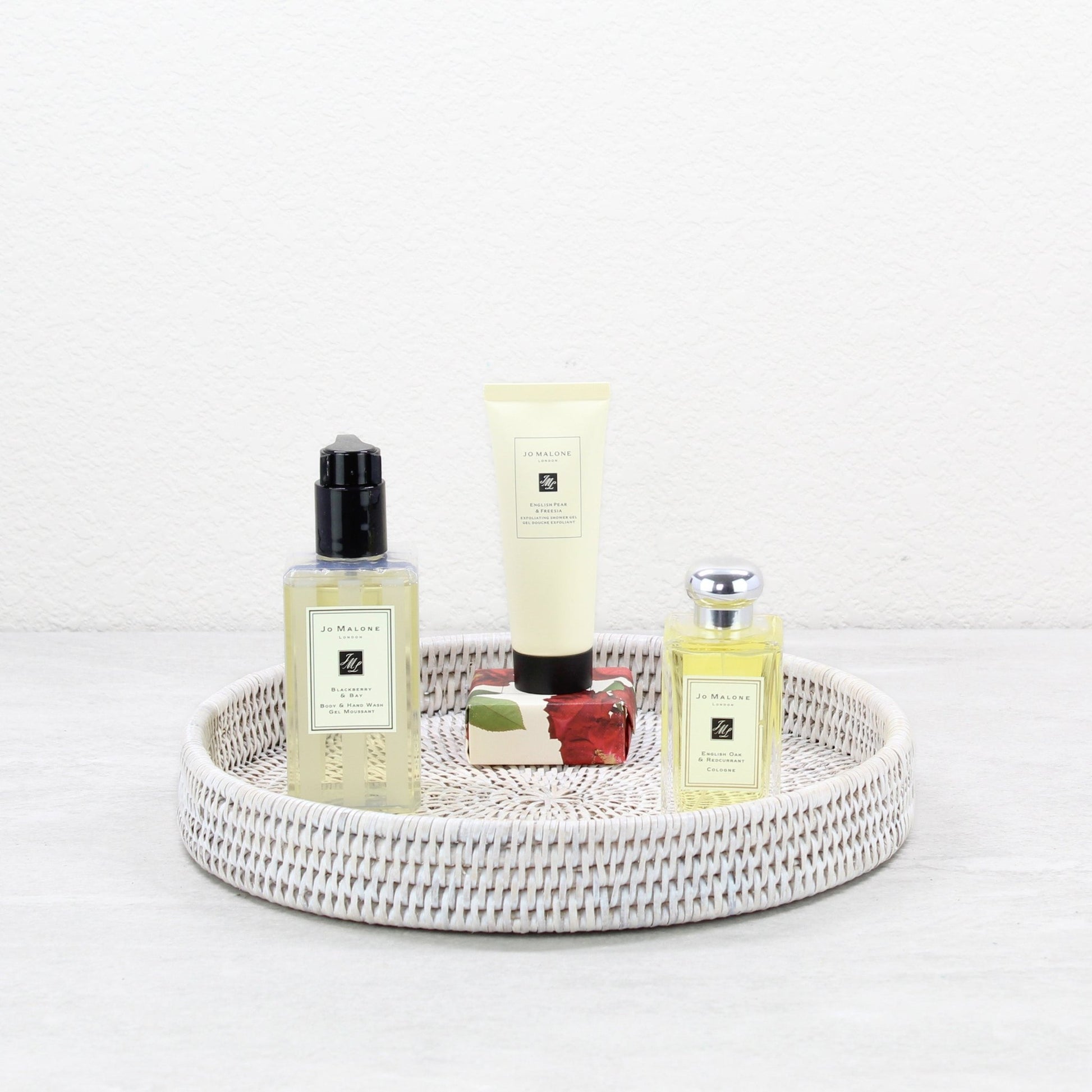 Round rattan tray in whitewash color styled with Jo Malone toiletries, sustainable luxury organizing tray.