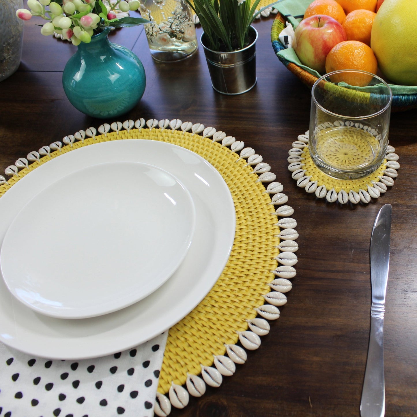 yellow seashell-trimmed rattan placemat used as charger under dinnerware, protecting tabletop and enhancing coastal presentation