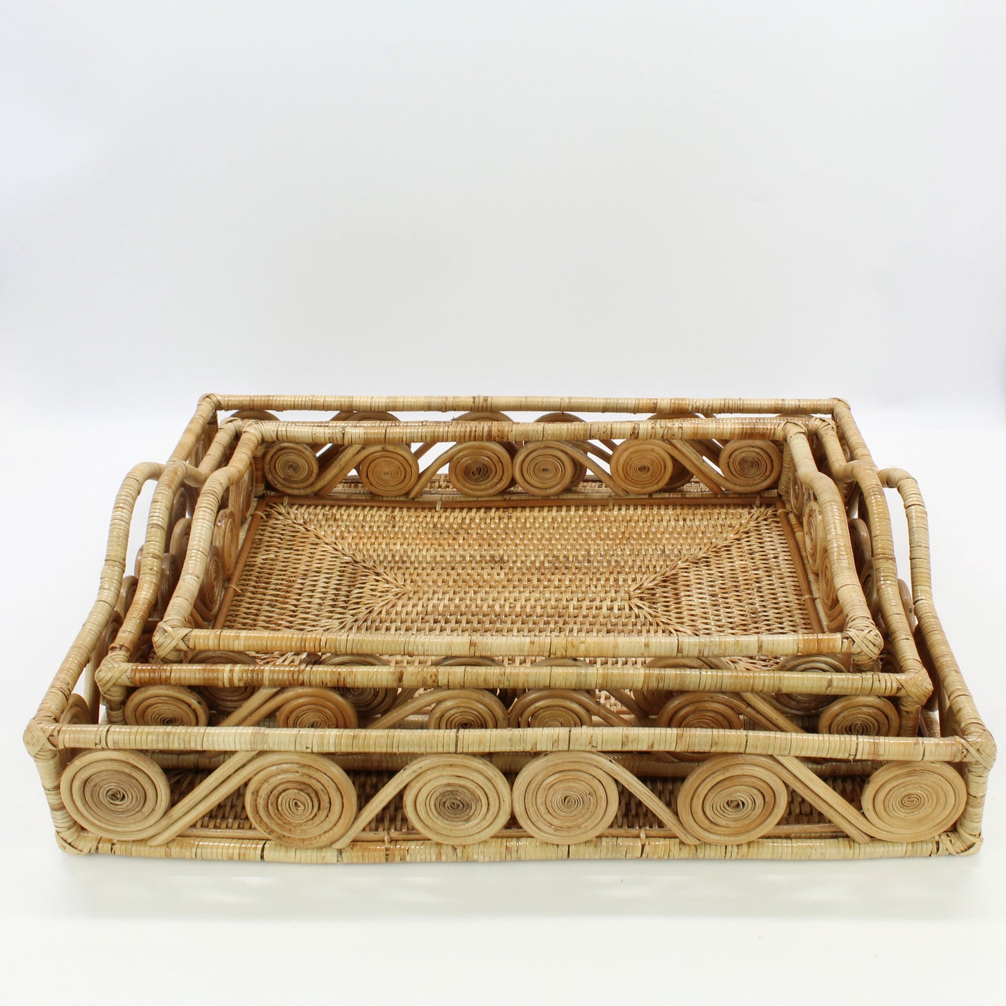 Set of natural rectangular rattan trays with swirl edge design, handmade and stacked in four sizes for versatile home organizing.