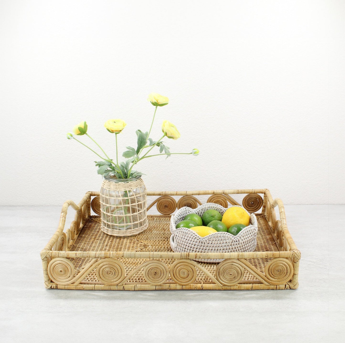 Natural rectangular rattan tray with swirl design, styled with a woven vase of yellow flowers and a white rattan bowl of lemons and limes.