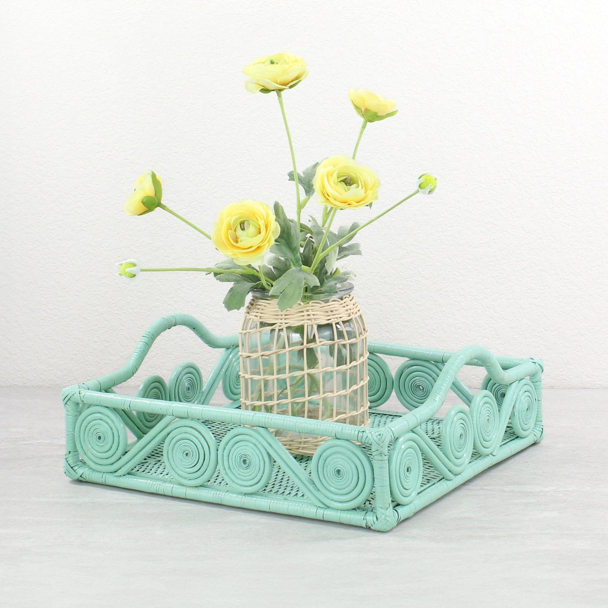 Sage leaf green rattan tray with swirl edge holding a blue floral vase of hydrangeas in front of a modern abstract painting