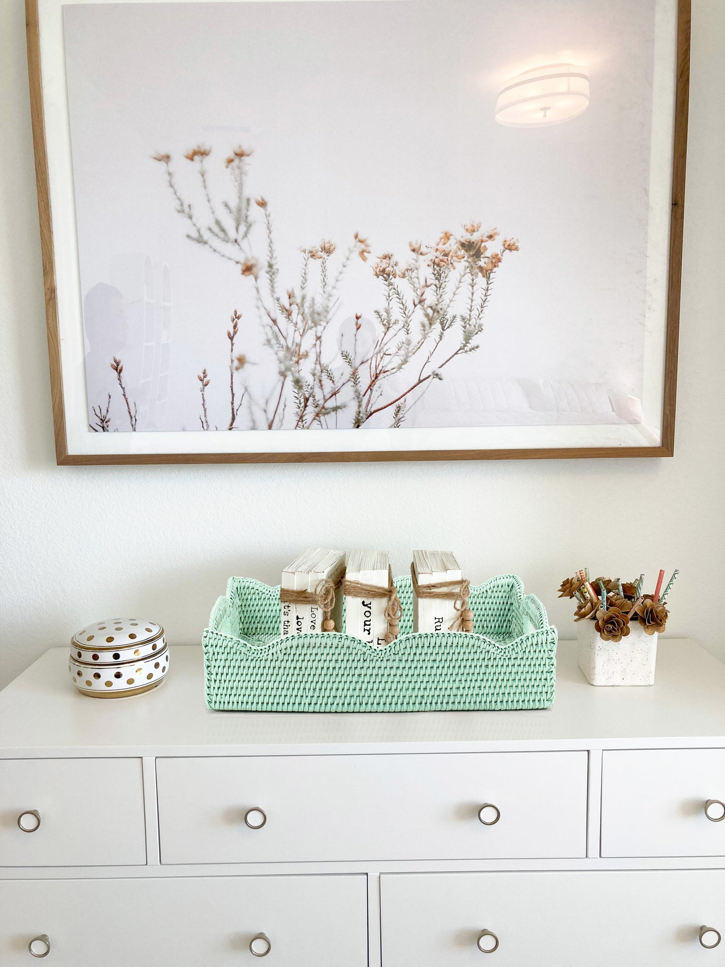 Sage leaf green scalloped rattan tray styled on a white dresser with rustic decorative books, eco-friendly handmade storage basket
