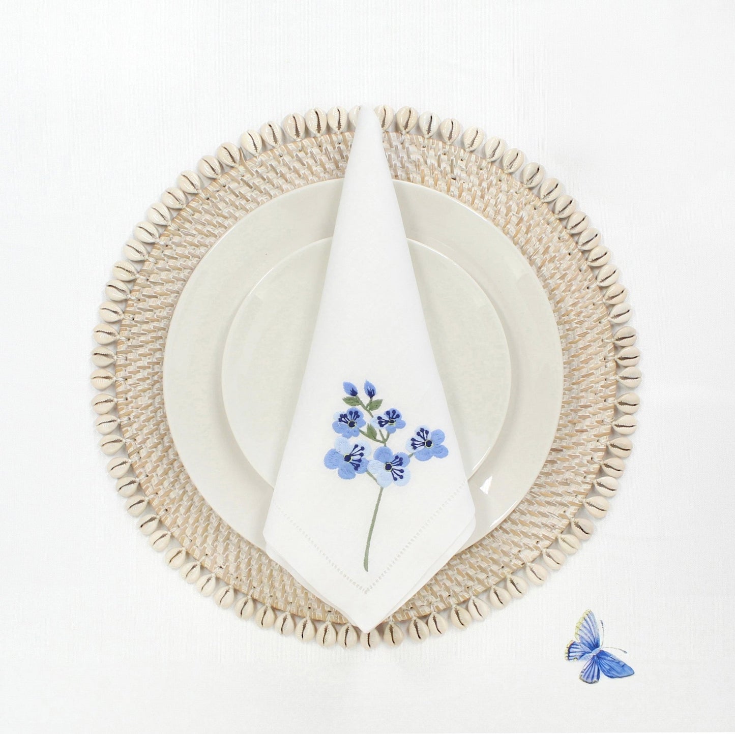 Handmade whitewash rattan placemat with natural seashell trim, shown with plate and napkin