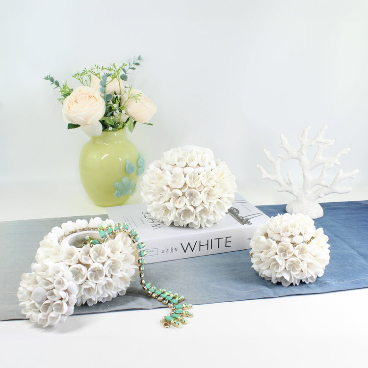Set of three handmade blossom seashell storage boxes with white tassels, displayed with roses in a green vase, artisan coastal home décor.