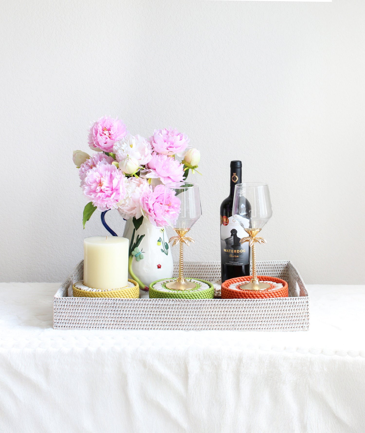Anniversary gift set styled with handwoven whitewash rattan tray, seashell coasters, hand-painted stoneware picture, and floral pitcher with pink flowers