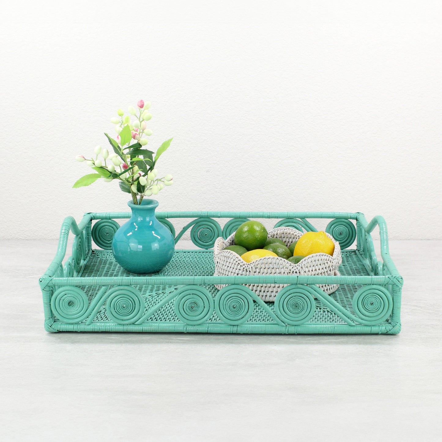 Turquoise rattan tray with swirl detail styled with a teal vase of flowers and a white rattan bowl of limes and lemons.