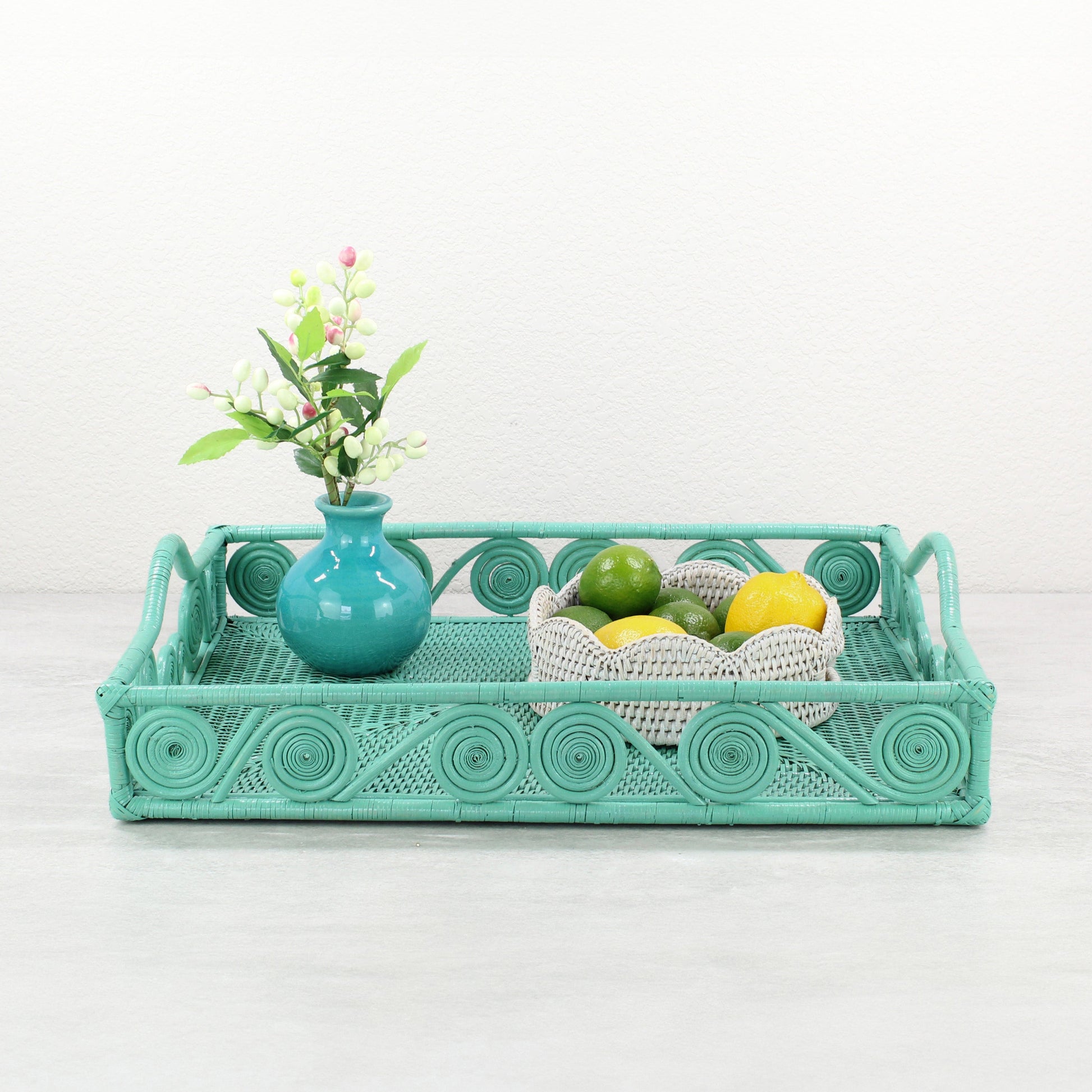 Turquoise rattan tray with swirl detail styled with a teal vase of flowers and a white rattan bowl of limes and lemons.