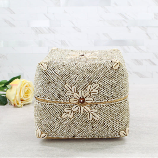 Large handcrafted beige beaded cowrie shell box with floral seashell pattern on the front, shown on a light modern surface.