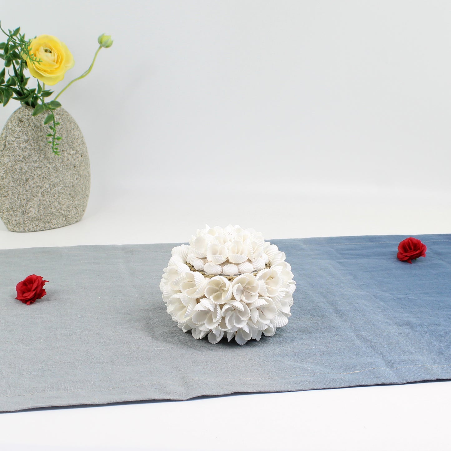 Small handmade seashell blossom decorative storage box with floral shell design, styled with a yellow flower vase and red rose accents for coastal décor.