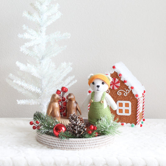 Handmade crochet polar bear toy and wooden penguin sculptures displayed on a whitewash rattan tray with festive holiday décor