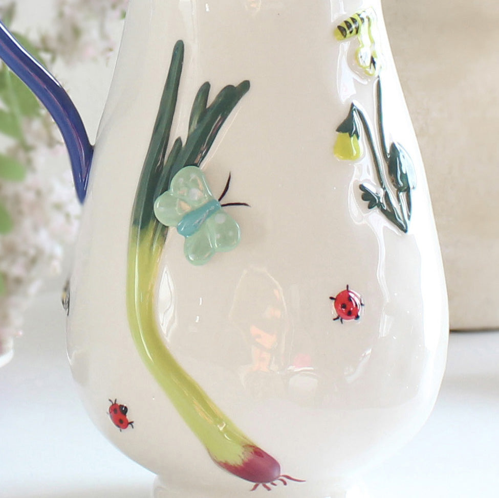 White stoneware pitcher with hand-painted garden-inspired motifs including flowers, butterflies, and ladybugs, artisan jug detailed view