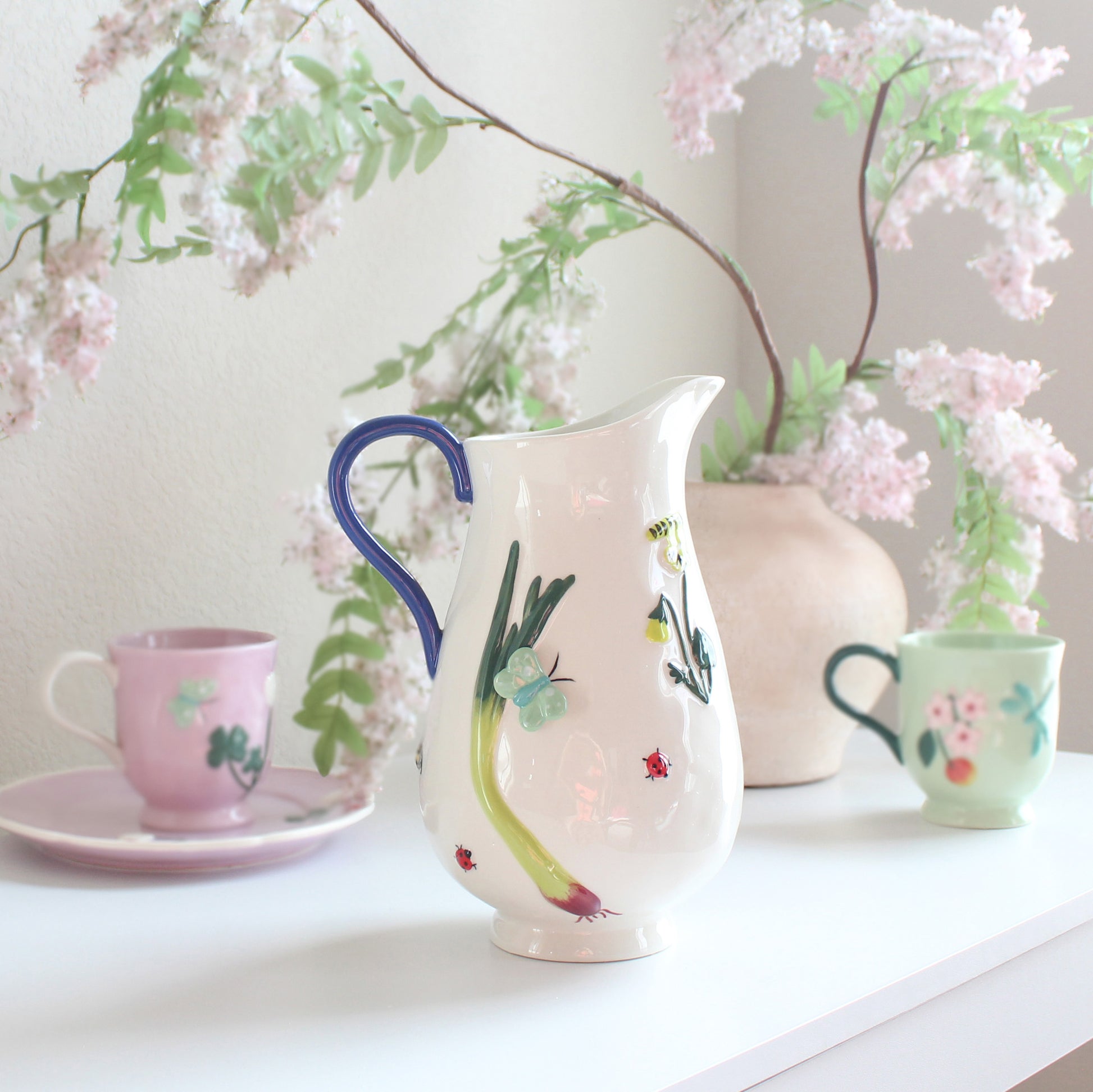White stoneware pitcher with hand-painted garden-inspired motifs including flowers, butterflies, and ladybugs, artisan jug, back view