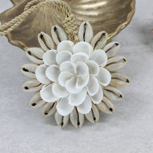 Handcrafted Bali seashell Christmas tree ornament with white cowrie and clam shells, woven raffia hanging cord, styled with gold dish background.