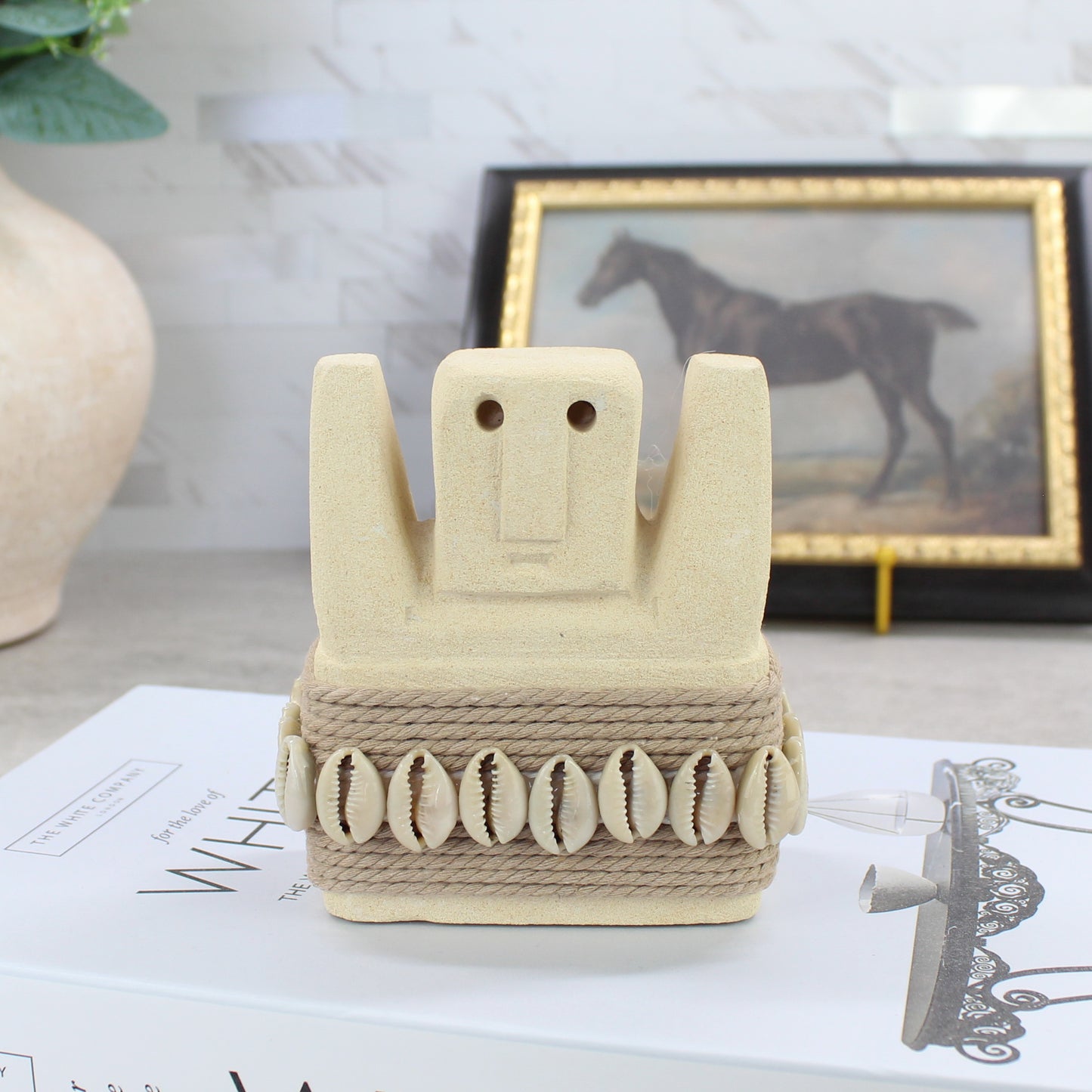 Handmade Sumba guardian statue with raised arms and cowrie shell belt on book - Balinese tribal decor.