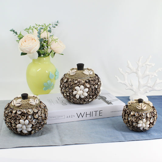 Set of three handmade cowrie and spiral seashell storage boxes with rope lids, displayed with vase and coral décor for coastal home styling.