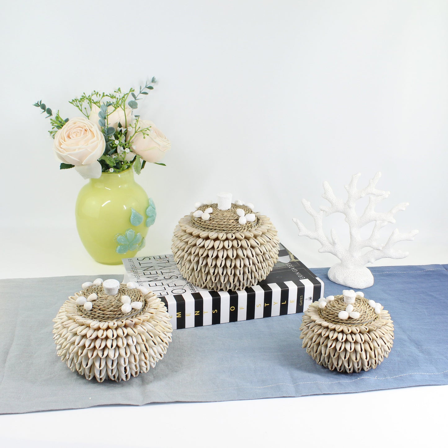 Handmade layered cowrie shell storage box with rope lid styled on a table with yellow roses – coastal jewelry and keepsake holder