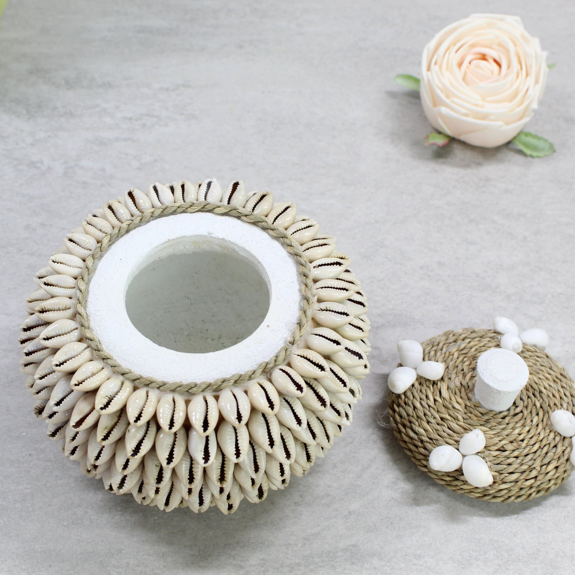 Handmade layered cowrie shell storage box with removable rope lid, showing interior design on neutral stone surface.