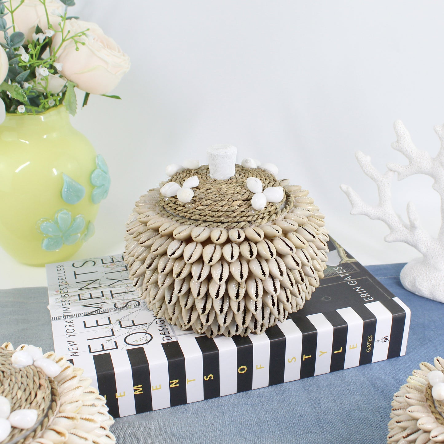 Layered cowrie shell jewelry and keepsake box with rope lid styled on design books for coastal home décor.