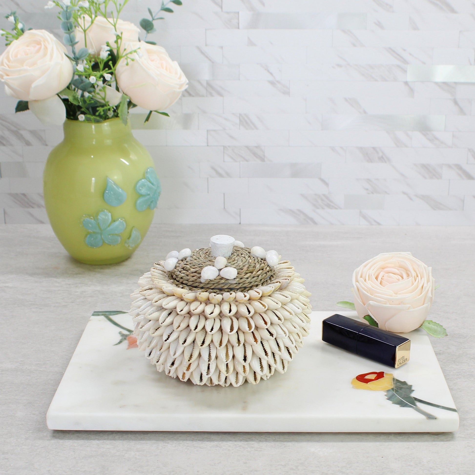 Handmade cowrie shell storage box styled with flowers and lipstick, ideal for vanity or dresser display.